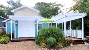 Une maison avec un porche couvert, un garage et un petit jardin agrémenté de plantes et d’un parasol jaune.