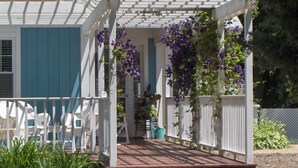 Une véranda couverte avec des balustrades blanches et des fleurs violettes.