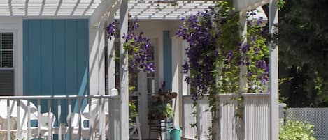 A covered porch with white railings and purple flowers.