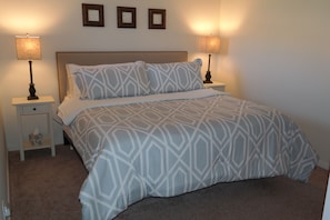 A neatly made bed with patterned bedding, two bedside lamps, and a small bedside table with a tissue box.