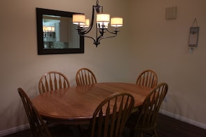 A dining room with a wooden table and chairs, a chandelier, a mirror, and a wall-mounted light switch.