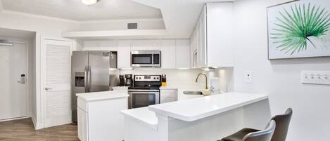 A modern kitchen with white cabinetry, stainless steel appliances, and a central island with two chairs.