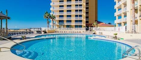 A swimming pool with a clear blue water, surrounded by a white fence and palm trees.