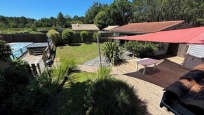 Un patio trasero con una terraza de madera, una parrilla, una piscina y un toldo rojo.
