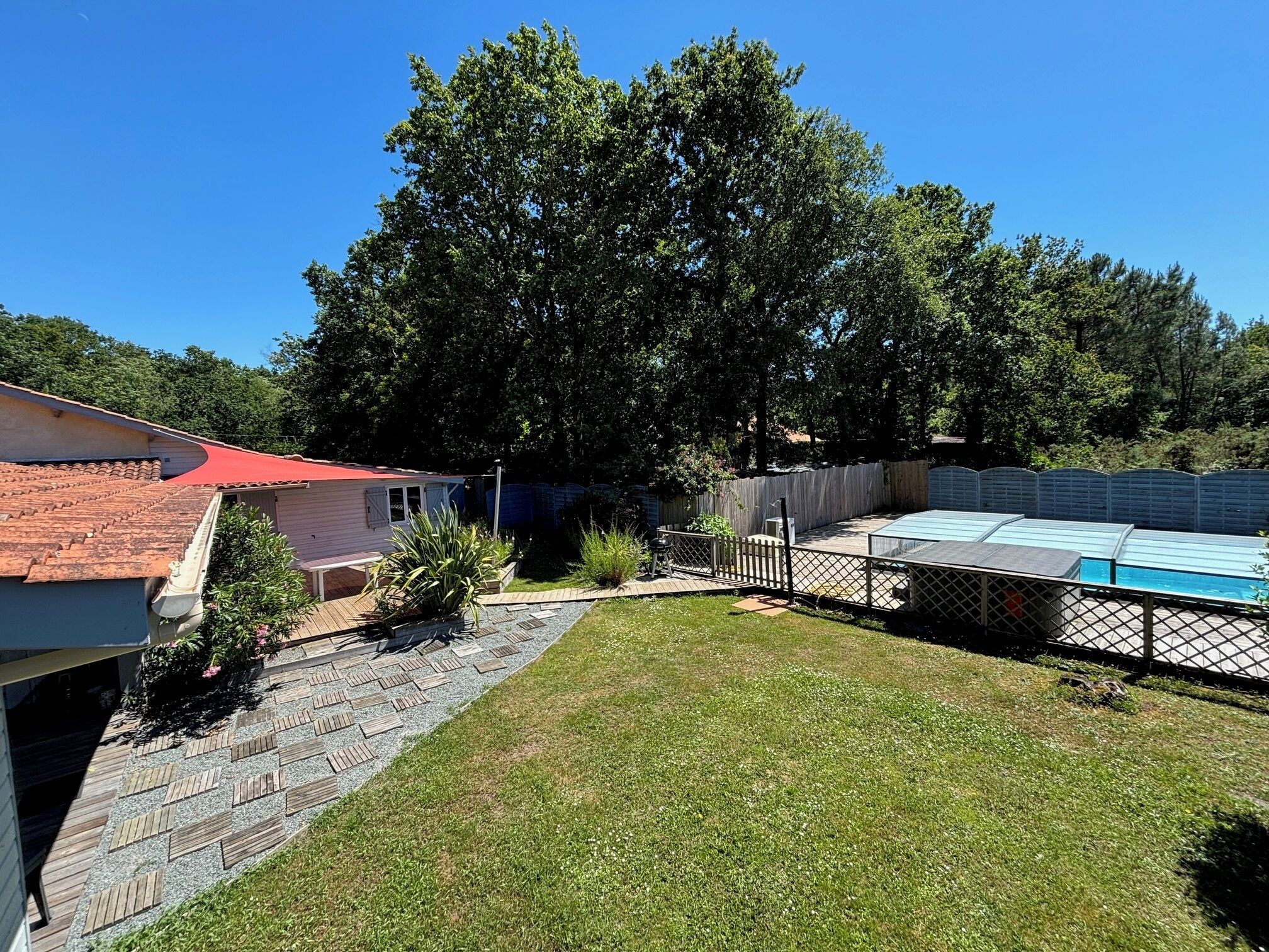 A backyard with a swimming pool, a wooden deck, and a house with a red roof.