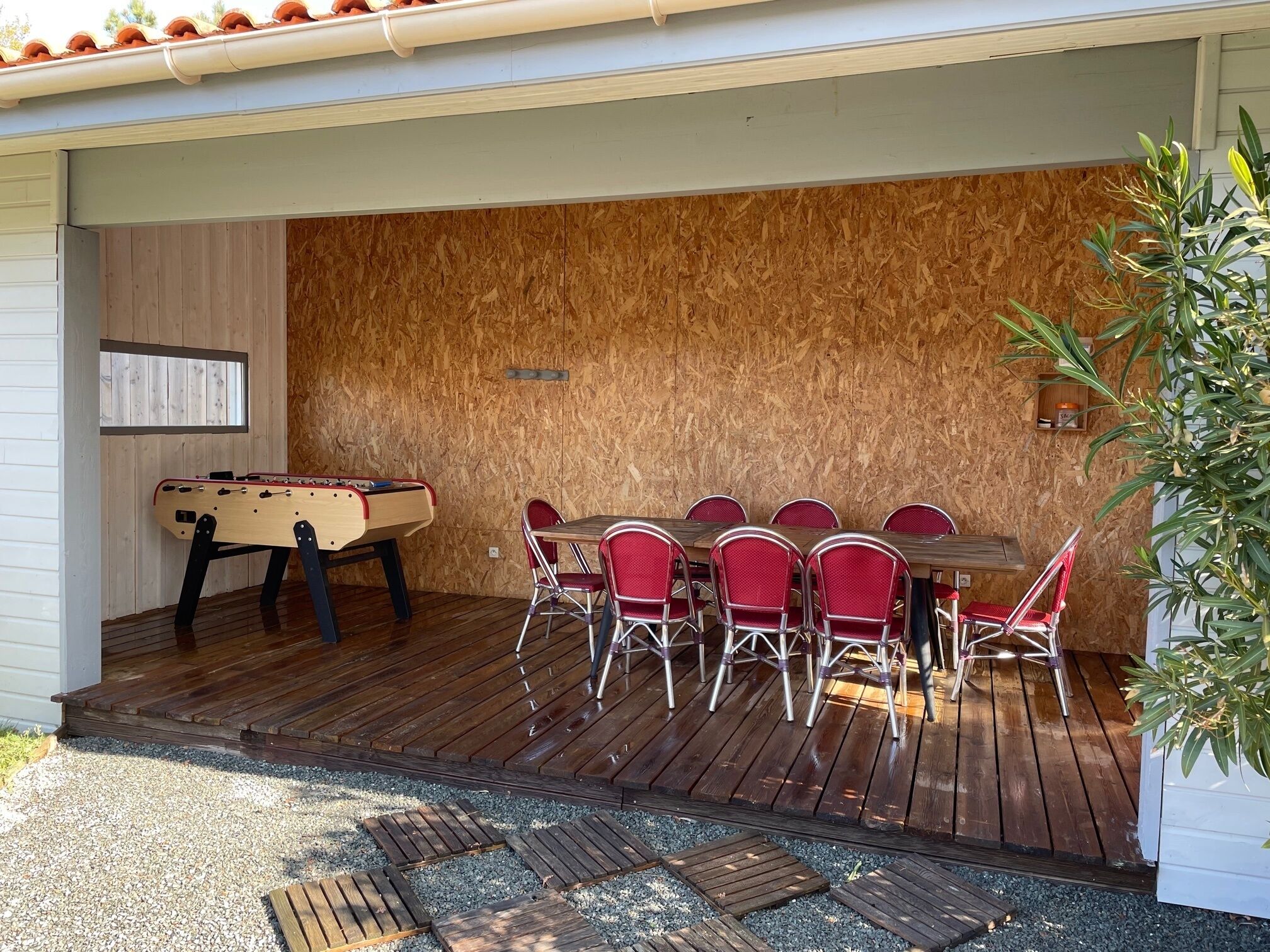 Eine Außenpatio mit Holzterrasse, einem Kicker und einem Esstisch mit roten Stühlen.