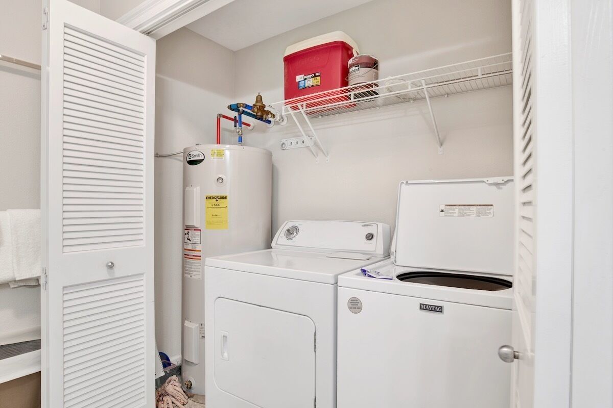 A laundry room with a white washer and dryer, a red storage box, and a water heater on a shelf.