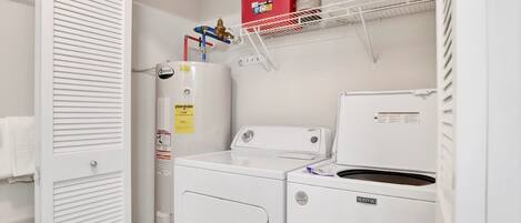 A laundry room with a white washer and dryer, a red storage box, and a water heater on a shelf.