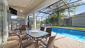 An outdoor patio with a glass table and chairs, a swimming pool, and a view of the backyard. - Olaf's Endless Summer at Windsor Hills (Kissimmee)