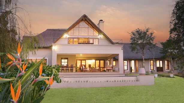 Een modern huis met een ruime veranda, een eethoek en een verzorgd gazon.