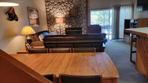 A dining area with a wooden table and chairs, a stone wall, a sofa, and a television in the background. - Snowcreek Resort Vacation Rental 596 (Mammoth Lakes)
