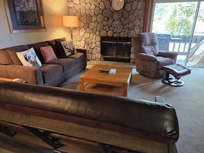 A living room with a stone wall, a fireplace, a sofa, a chair, and a coffee table. - Snowcreek Resort Vacation Rental 596 (Mammoth Lakes)