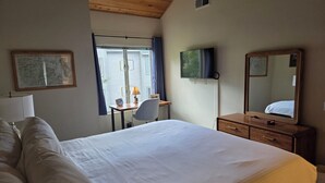 Hotellihuone, jossa on suuri sänky, työpöytä tuolilla, televisio, lipasto ja ikkuna, jossa on verhot.