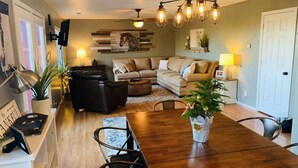 A modern living room with a wooden dining table, leather sofa, and a chandelier. - Mountain View Retreat Close to Downtown Flagstaff, Big Deck, Trails Nearby! (Flagstaff)