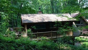 A rustic cabin with a wooden deck and a chimney, surrounded by dense forest. - Cozy Cabin in The Driftless (Cross Plains)