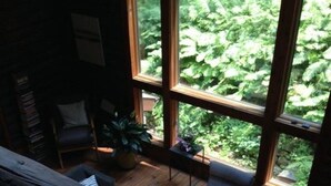 A cozy room with a large window, a wooden floor, a sofa, a small table, and a chair. - Cozy Cabin in The Driftless (Cross Plains)