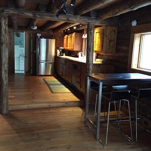 A rustic kitchen with wooden cabinets, a stainless steel refrigerator, and a bar area with stools.