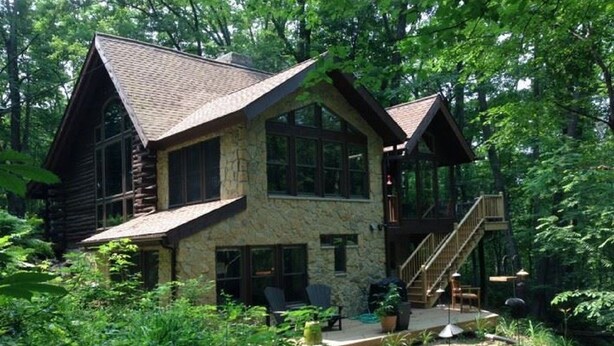 A two-story log cabin with a stone facade, large windows, and a deck with outdoor seating. - Cozy Cabin in The Driftless (Cross Plains)