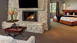 A stone fireplace with a TV above it, a bed with a wooden headboard, and a nightstand with a lamp and flowers.
