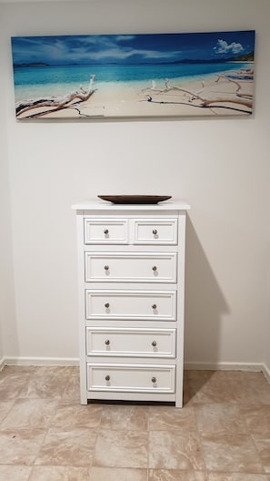 A stylish chest of drawers sits against the wall, accompanied by a serene beach scene above.