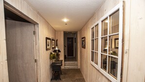 A hallway with wooden walls, a stone floor, a desk with a lamp, and a door leading to another room. - Goetzl by Hauserman Rental Group (Tahoma)