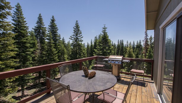 A wooden deck with a round table and chairs, a grill, and a scenic view of tall trees. - Goetzl by Hauserman Rental Group (Tahoma)