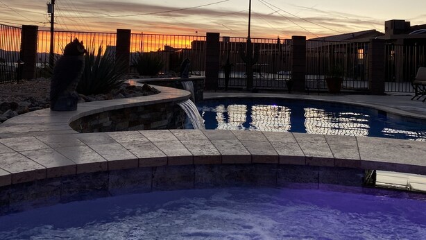 A swimming pool with a waterfall feature, surrounded by a fence and a view of a sunset. - Spacious Santa Fe 4b/4b Pool and Spa home centrally located (Lake Havasu City)