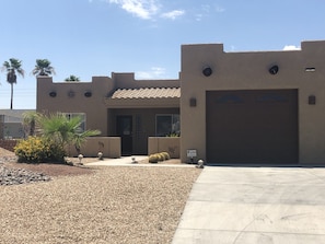 Stylish residential building with a flat roof, central entrance, and garage door, set amidst a beautifully landscaped garden with palm trees and shrubs.