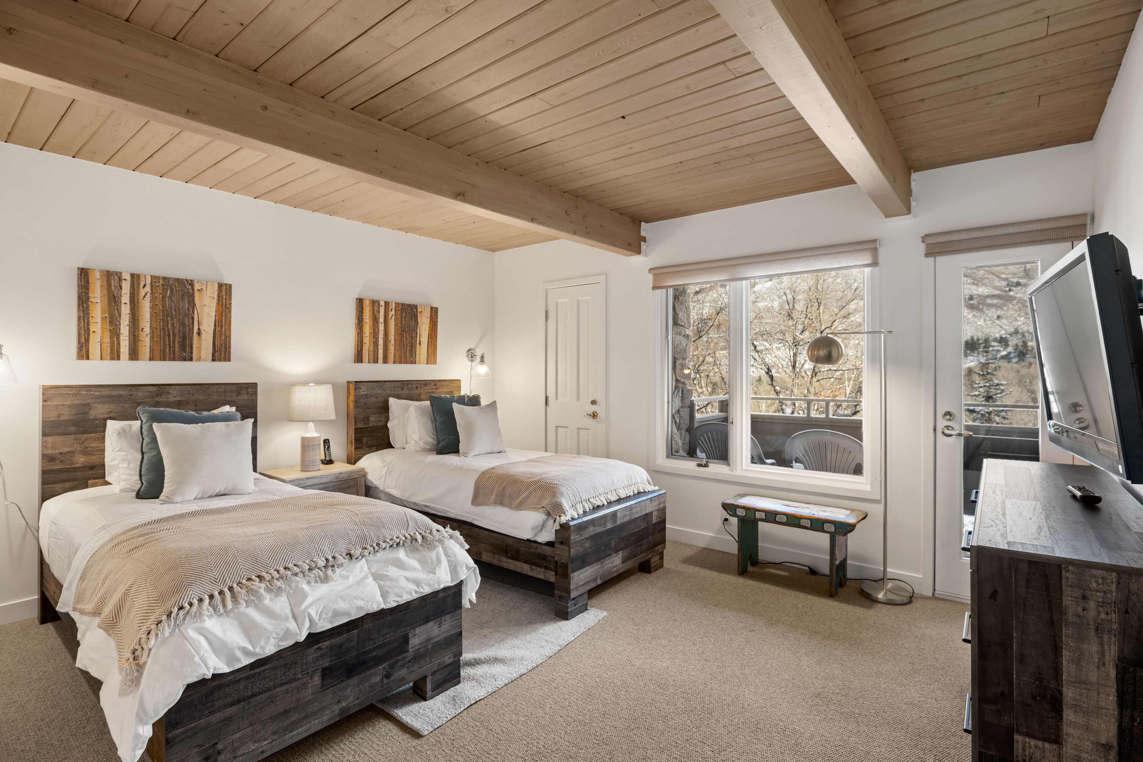 A bedroom with two beds, wooden headboards, a large window with a view, and a TV on a wooden dresser.