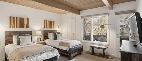 A bedroom with two beds, wooden headboards, a large window with a view, and a TV on a wooden dresser.