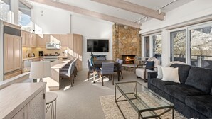 Un espace de vie et de salle à manger moderne, à aire ouverte, avec une cheminée en pierre, de grandes fenêtres et un coin salon confortable.
