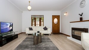 A living room with a sofa, a coffee table, a TV, a fireplace, and a door with a window. - Adelaide Style Accommodation - Getaway-Close to City In elite North Adelaide (North Adelaide)