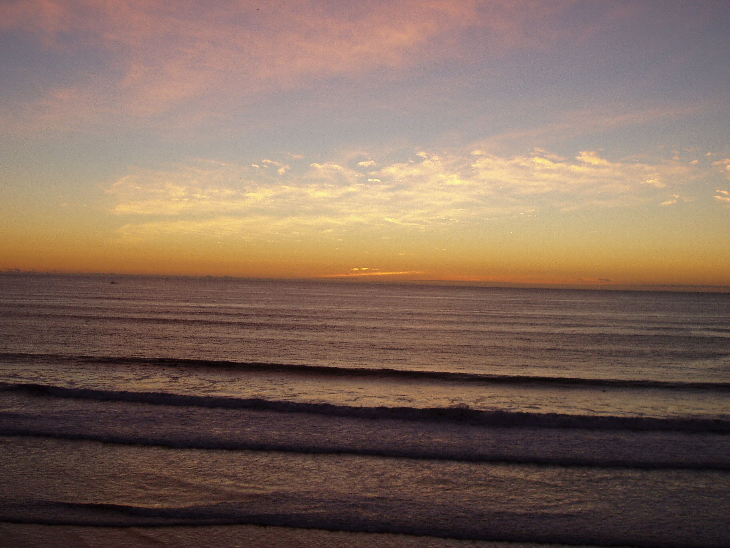 A beach with calm waves and a sunset in the background.