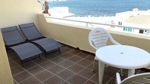A balcony with two lounge chairs and a small table, overlooking a body of water and a distant pier. - Villa with private pool, terraces and direct access to the sea +Wifi (Corralejo)