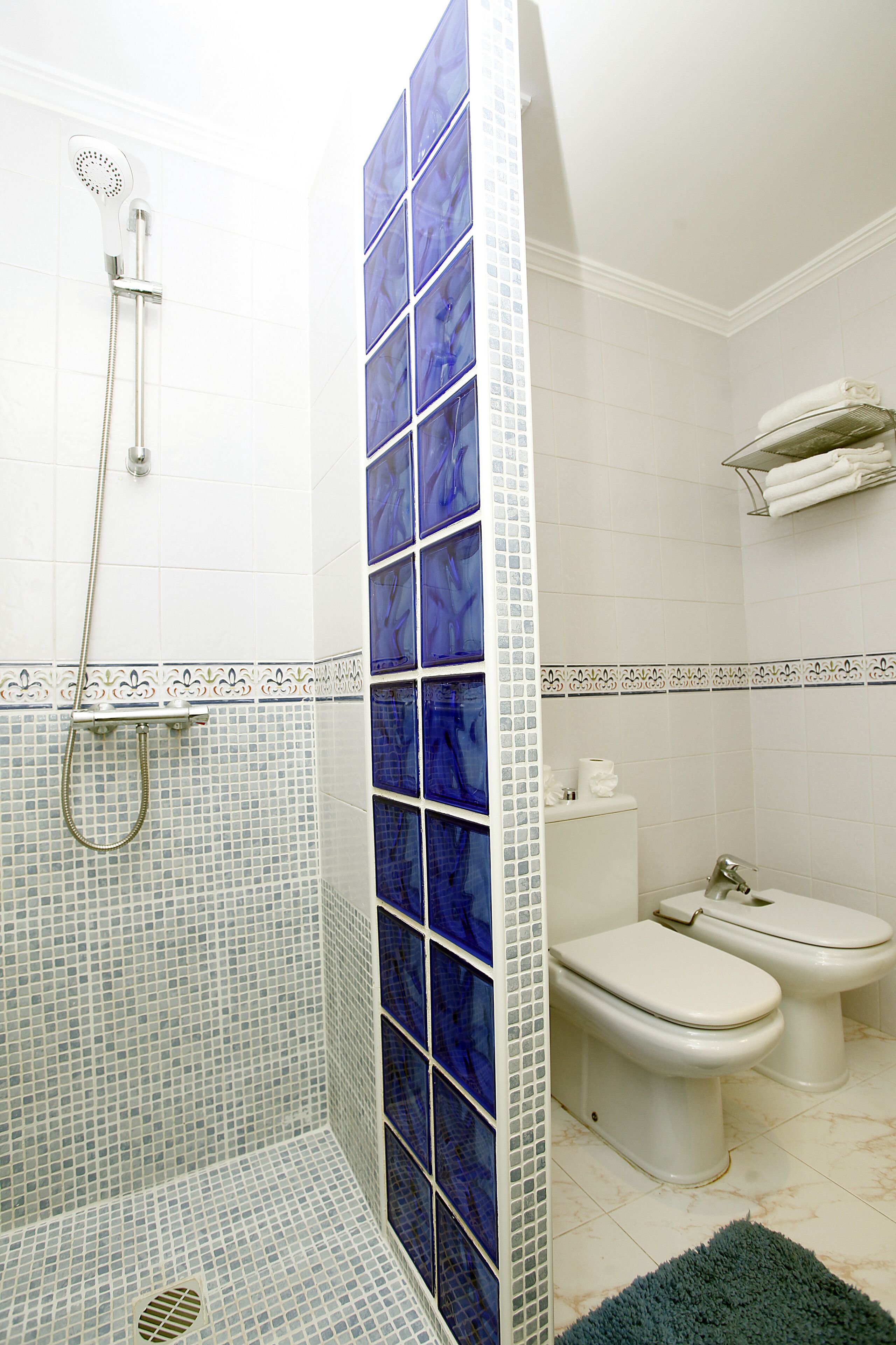 A bathroom with a shower, two toilets, and a towel rack.