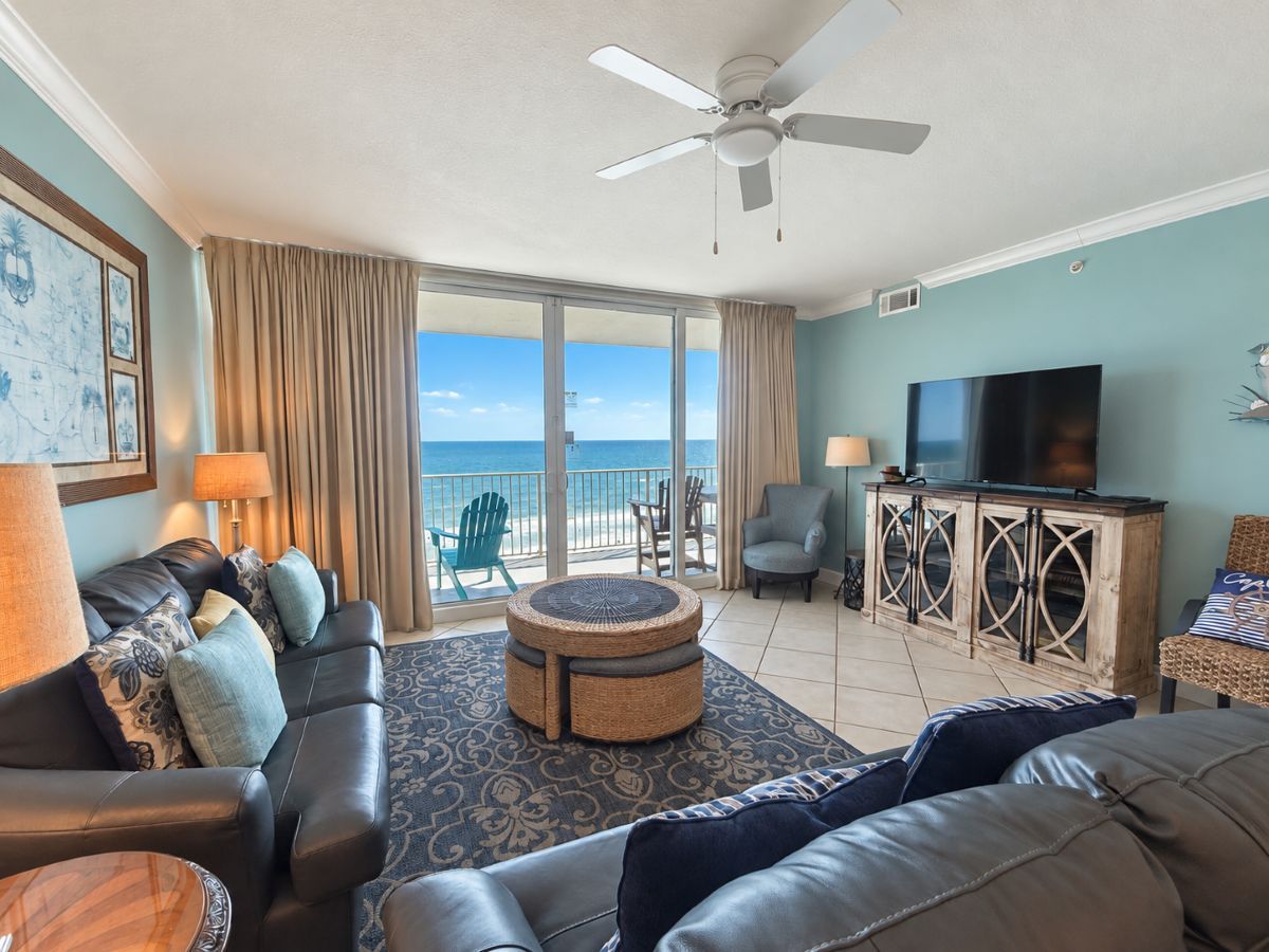 A living room with a sofa, armchairs, a coffee table, a television, and a balcony with a view of the ocean.