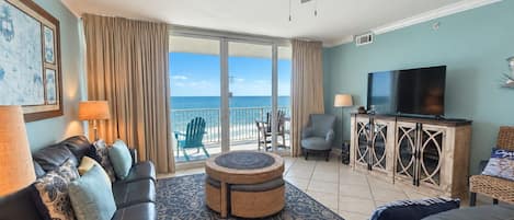 Ein Wohnzimmer mit Sofa, Sesseln, einem Couchtisch, einem Fernseher und einem Balkon mit Meerblick.