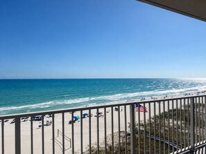 A beach view from a balcony with a railing, ocean, and beachgoers. - Modern Beachfront Condo w/ Corner Views & Pool | Sleeps 10 (Gulf Shores)