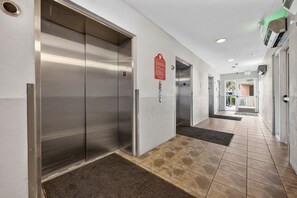 Corredor com dois elevadores, um sinal de segurança contra incêndio e uma porta que dá para área externa.