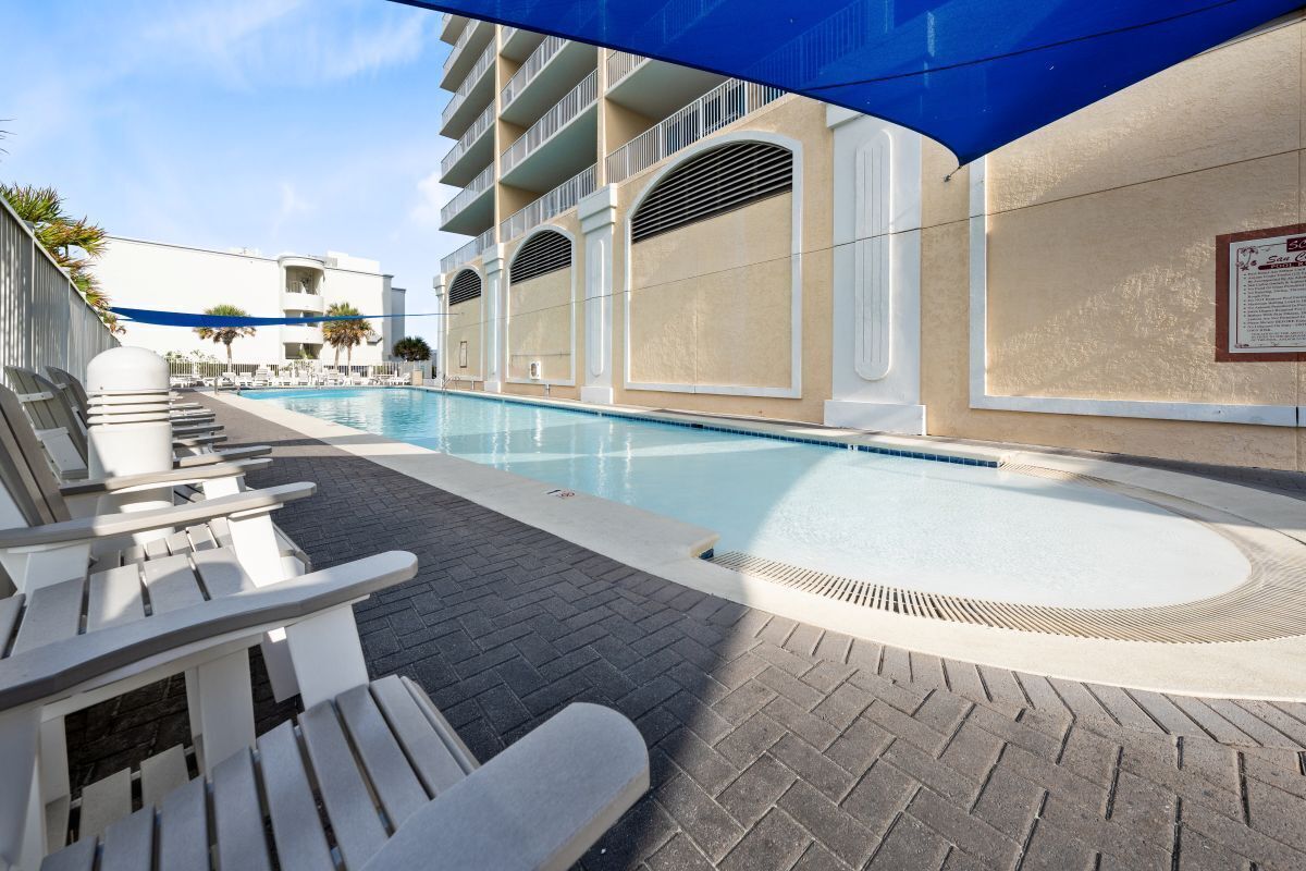 Ein Swimmingpool mit Liegestühlen und einem überdachten Bereich, angrenzend an ein Gebäude mit Balkonen.