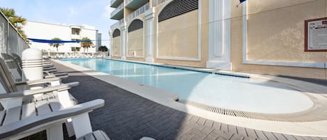 Ein Swimmingpool mit Liegestühlen und einem überdachten Bereich, angrenzend an ein Gebäude mit Balkonen.