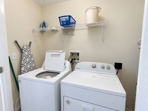 A laundry room with two white washers and dryers, a blue laundry basket, and a white bucket on a shelf. - Modern Beachfront Condo w/ Corner Views & Pool | Sleeps 10 (Gulf Shores)