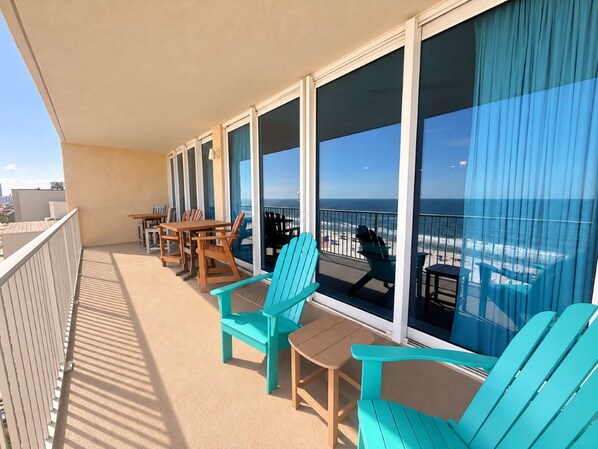 A balcony with a view of the beach, equipped with chairs and tables.