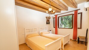 A bedroom with two single beds, a wooden ceiling, a window with curtains, and a bedside table with a lamp. -  Cottage with private pool, free WIFI, mountain views and huge garden. (Campanet)