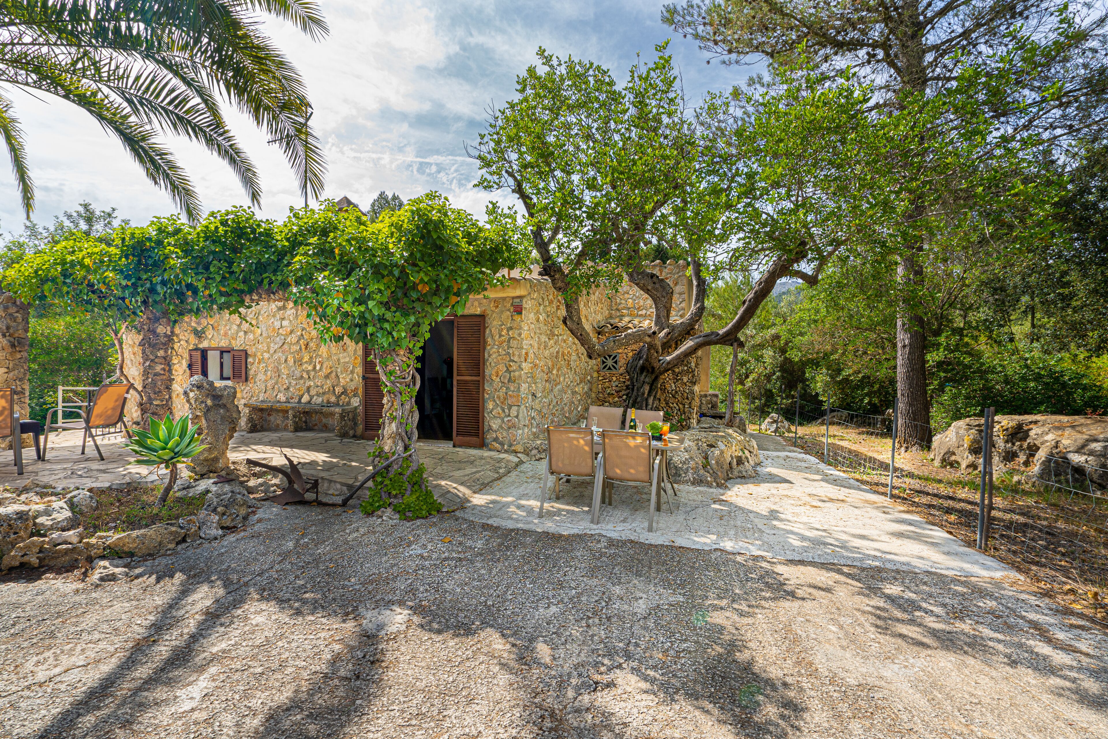 A rustic stone building with a wooden door, surrounded by trees and a gravel path.