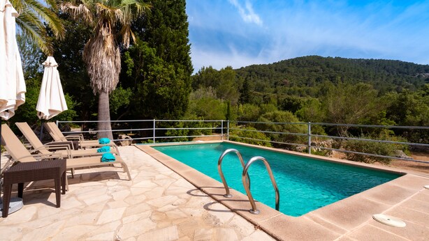 A swimming pool with lounge chairs and umbrellas, surrounded by trees and a hilly landscape. -  Cottage with private pool, free WIFI, mountain views and huge garden. (Campanet)