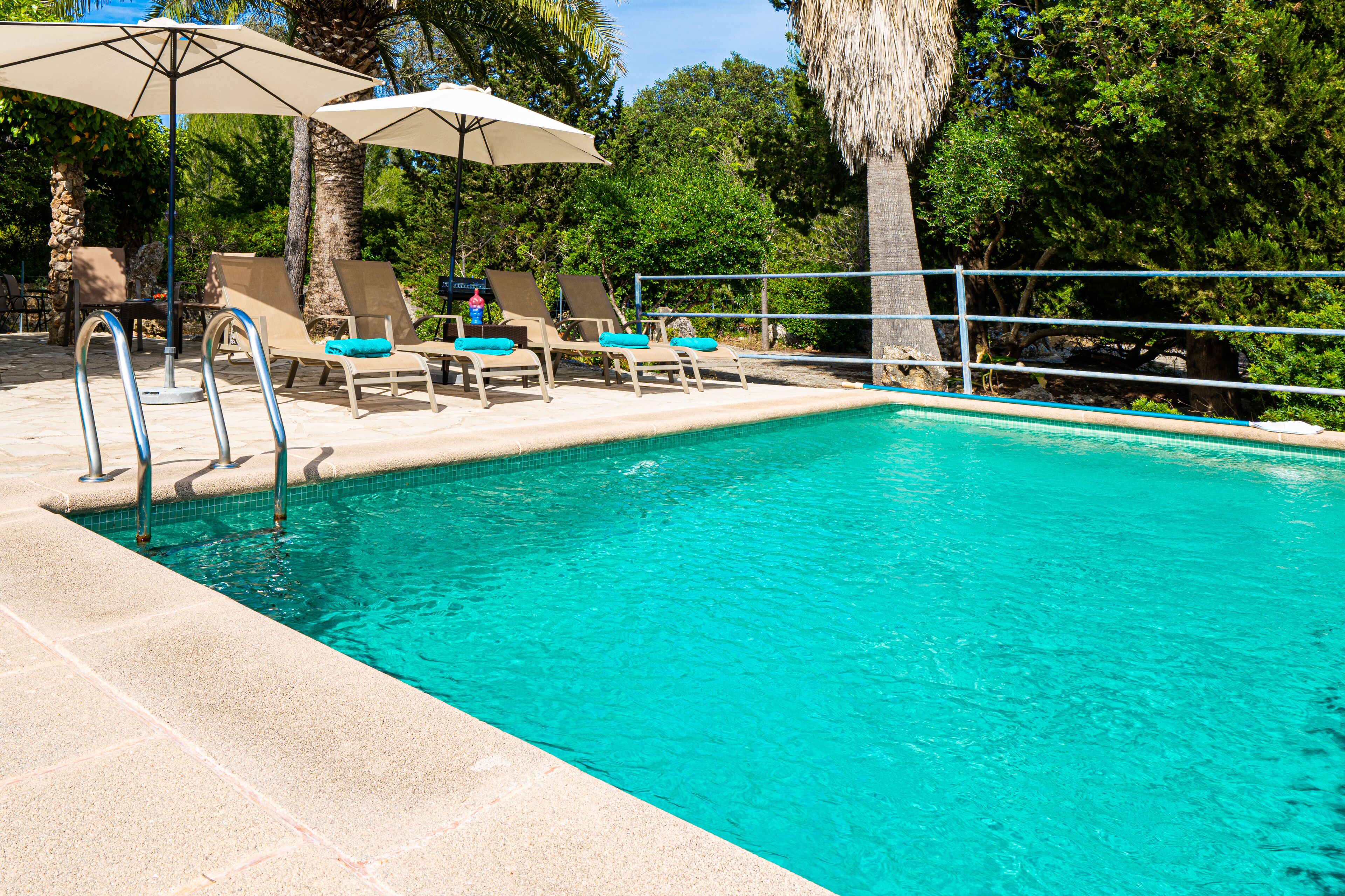 A swimming pool with lounge chairs and umbrellas, surrounded by trees and a stone wall.