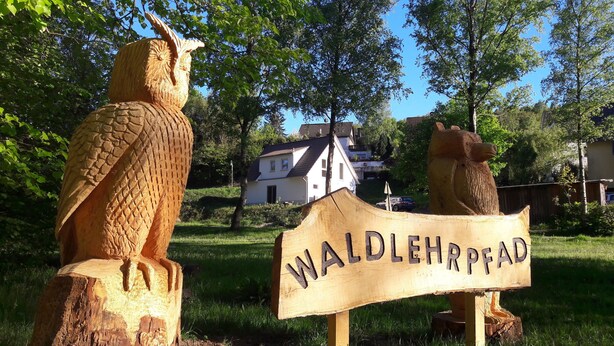 A wooden sign with the text "WALDEHRPPAAD" in a rural setting with two wooden sculptures, one of a bird and one of a bull, and a house in the background. - Vacation home QUELLENHAIN with 5 bedrooms, 2 bathrooms, 3 terraces, garden (Reichshof)