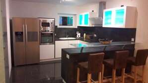 A modern kitchen with a central island, bar stools, stainless steel appliances, and a window above the sink. - Vacation home QUELLENHAIN with 5 bedrooms, 2 bathrooms, 3 terraces, garden (Reichshof)