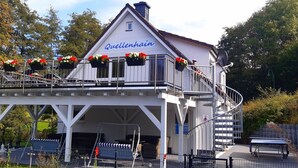 A building named Quellenhain with a balcony, outdoor seating, and flower baskets. - Vacation home QUELLENHAIN with 5 bedrooms, 2 bathrooms, 3 terraces, garden (Reichshof)